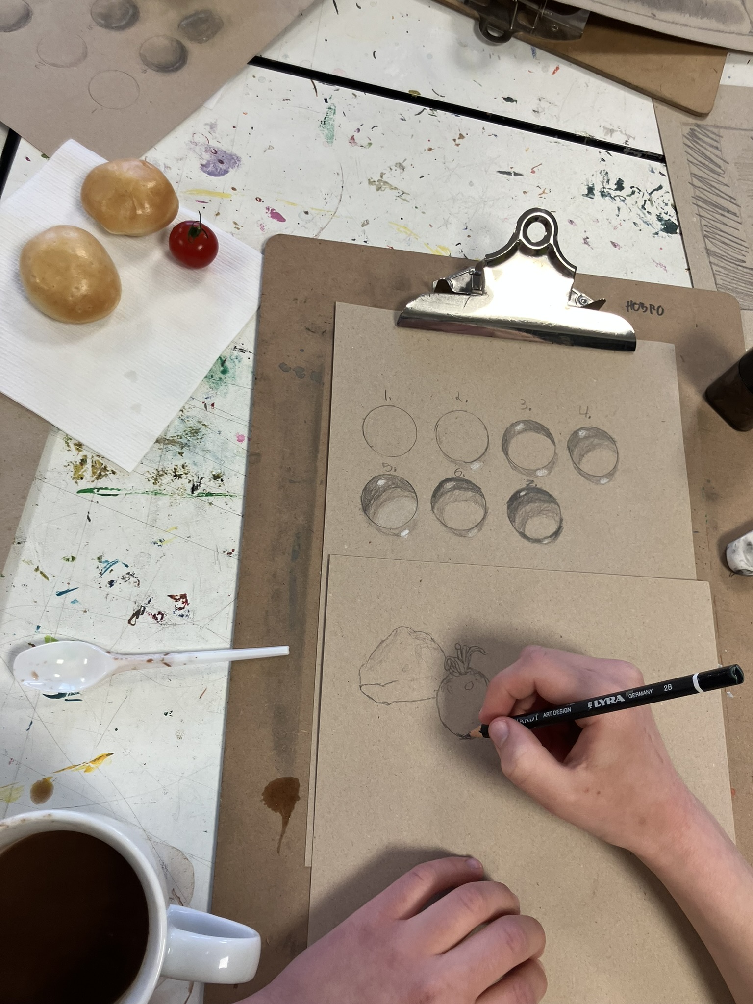 Blyanttegning ligger på borden mens man ser en hånd tegne på det